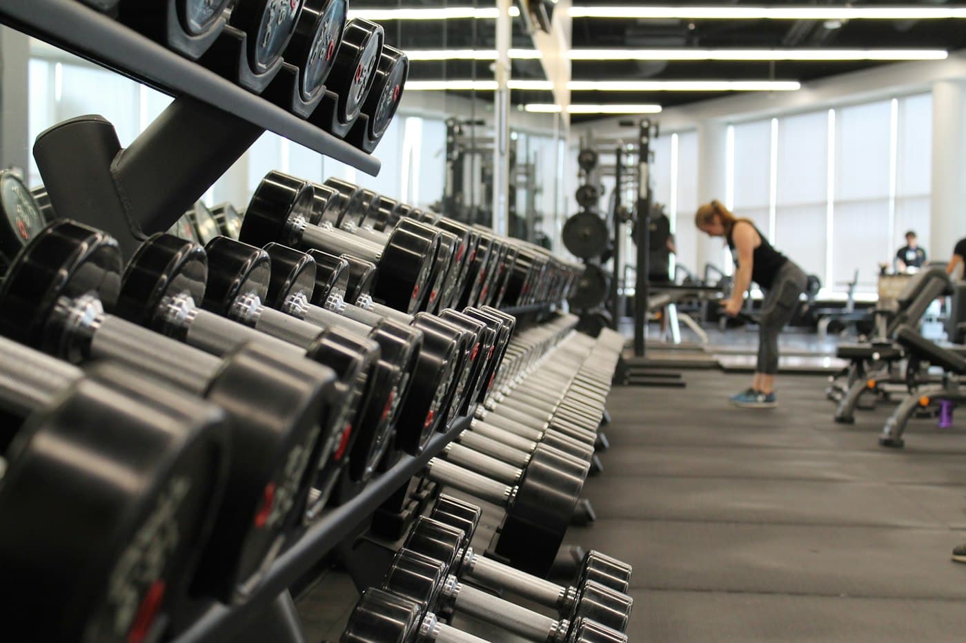 Sala de musculação com rack de halteres e alunos treinando